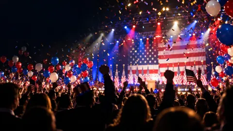 Election night crowd celebrating under red, white, and blue balloons and confetti